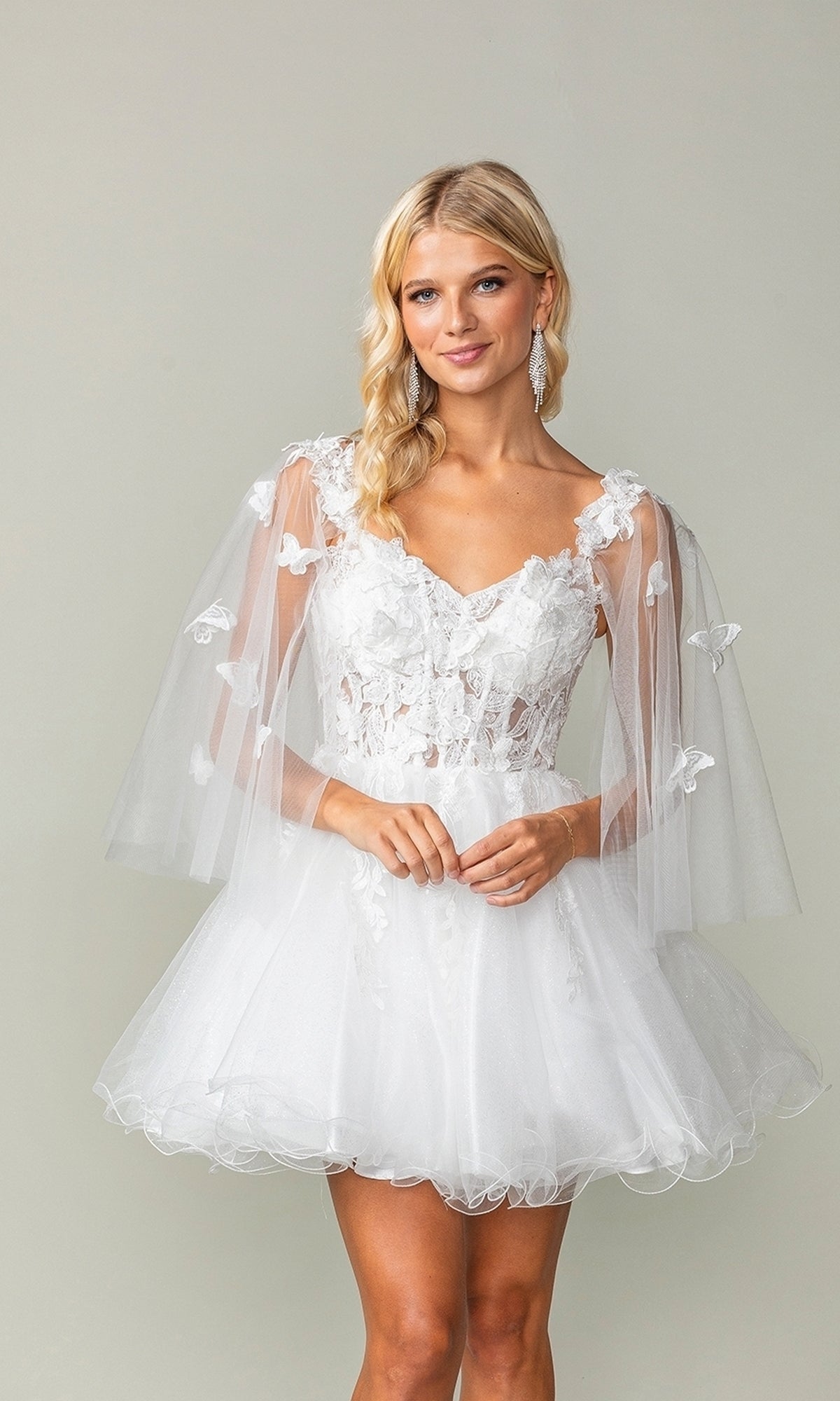 A woman models the Butterfly-Cape Short A-Line Homecoming Dress 3393, featuring floral lace, sheer butterfly capelet sleeves, and a tulle skirt, against a plain light background.